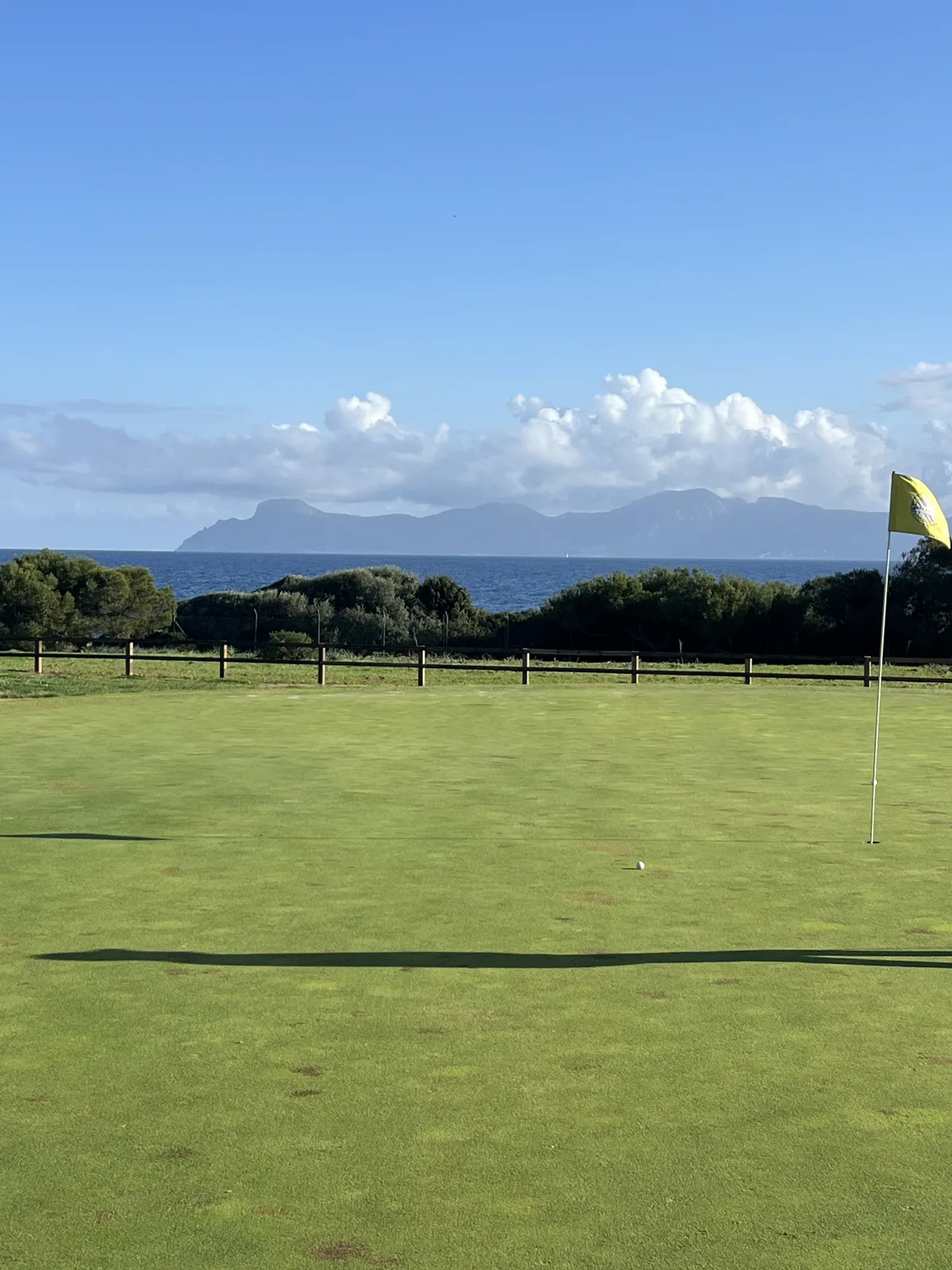 A flag on the green at Alcanada with the sea and mountains behind