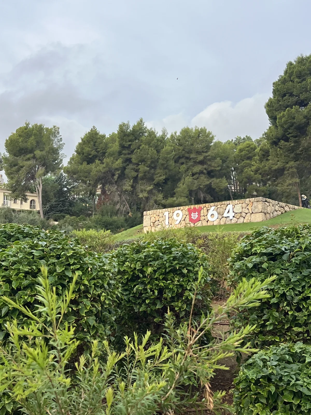 Steinmauer mit der Zahl 1964 und dem Wappen von Son Vida zwischen Bäumen auf dem Golfplatz Son Vida, Mallorca
